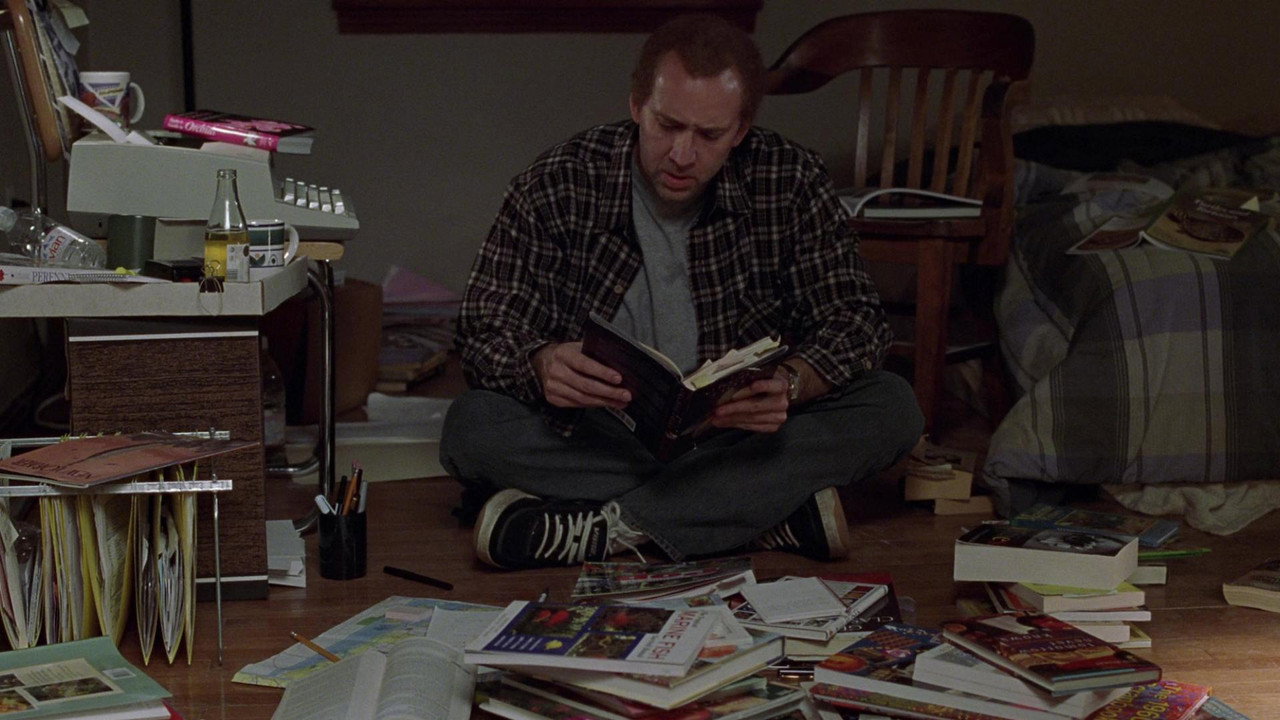Charlie Kaufman sitting cross-legged on the floor, buried in research books